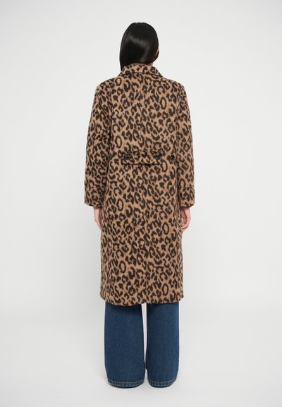 Cappotto leopardato in tonalità sabbia e marrone, con colletto strutturato, maniche lunghe e vita con cintura. Abbinato a pantaloni di denim a gamba larga.