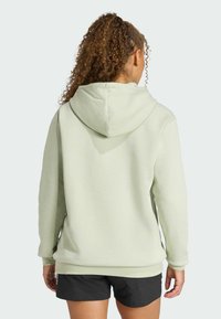 Jasnozielona bluza z kapturem o gładkiej fakturze, z długimi rękawami i luźnym krojem, w zestawieniu z czarnymi szortami.