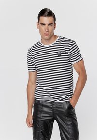 Czarna i biała koszulka w paski z okrągłym dekoltem, krótkimi rękawami i małym okrągłym logo na piersi. W połączeniu z eleganckimi czarnymi spodniami.