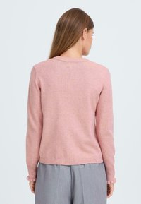 Różowy, dzianinowy sweter z długimi rękawami, ściągaczami na mankietach oraz okrągłym dekoltem, charakteryzujący się miękką fakturą i lekko strzępionym dołem.
