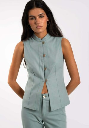 Top sin mangas de color verde menta con un cuello alto, cierre frontal de botones, costuras verticales y un dobladillo dividido. La tela parece suave con un ligero brillo.
