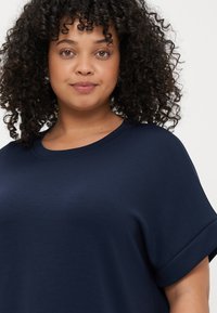 Μπλέ νάυ με oversized T-shirt φτιαγμένο από μαλακό ύφασμα, διαθέτοντας στρογγυλή λαιμόκοψη και γυρισμένα μανίκια για άνετη εφαρμογή.