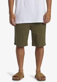 Olijfgroene shorts van katoen, met een rechte snit, opgerolde zoom en zijzakken, gecombineerd met bruine instapsandalen en een wit T-shirt.
