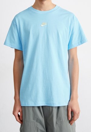 T-shirt en coton bleu avec des manches courtes, un col rond et un petit logo Nike jaune brodé sur la poitrine. Texture lisse.