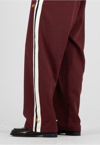 Burgundské široké nohavice s bielymi a námorníckymi pruhmi po stranách. Majú zlatú výšivku a sú skombinované s čiernymi textúrovanými topánkami.