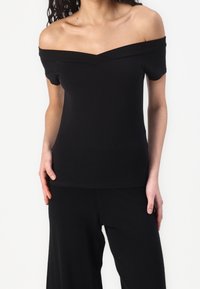 Černý top bez ramínek vyrobený z hladké, elastické tkaniny s přiléhavým střihem, vybavený výstřihem ve tvaru V a krátkými rukávy.