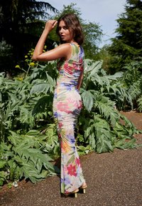 Rochie colorată cu imprimeu floral, realizată dintr-un material elastic, cu pliuri pe laterale și o siluetă ajustată, având o fustă lungă până la glezne.