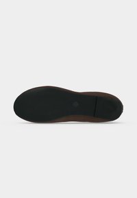 Semelle d'une chaussure plate marron avec une surface en caoutchouc noir texturé et un petit logo circulaire près du centre.