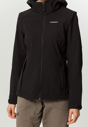 Zwarte softshell jas met rits, capuchon en voorzakken met rits, gedragen met beige broek, toont alleen torso en armen.