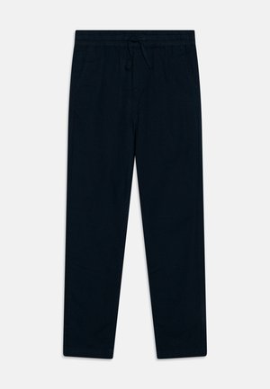Pantalones de algodón azul marino con corte slim, que cuentan con bolsillos laterales y una textura suave, combinados con zapatillas oscuras. Camisa a rayas visible por encima.