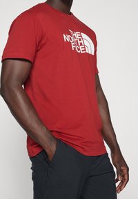 Red short-sleeve t-shirt in cotton with a crew neck, featuring a prominent white logo of "The North Face" on the front.
