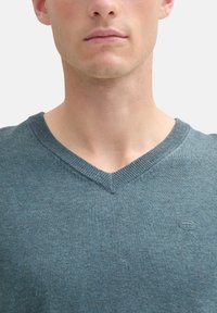 Pullover con scollo a V in verde teal tenue, realizzato in un morbido tessuto a maglia. Presenta un colletto a coste e un piccolo logo sul petto.