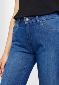 Jeans de mezclilla azul con estilo de cinco bolsillos, cierre de botón y un ligero desgastado. Presenta un corte recto clásico y una cintura de altura media.