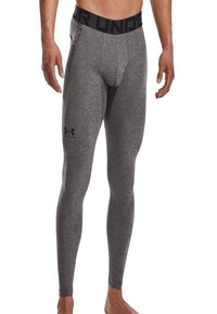 Grijze, strakke sportleggings met een zwarte elastische tailleband. Kenmerken zijn een gladde textuur en een logo op de dij.