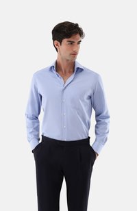 Hellblaues Langarmhemd aus Baumwollmischung mit spitzem Kragen, Fronttasche und Knopfleiste, kombiniert mit dunklen Hosen.