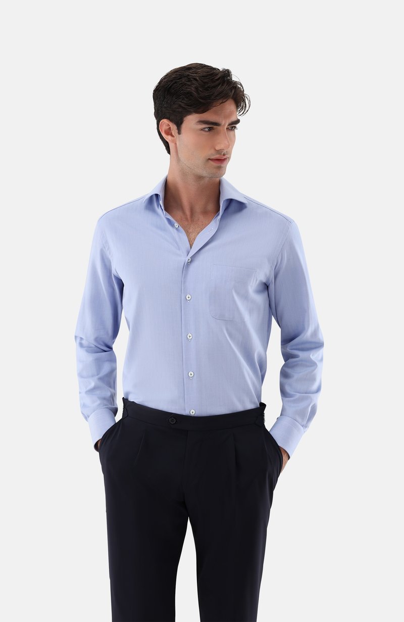 Hellblaues Langarmhemd aus Baumwollmischung mit spitzem Kragen, Fronttasche und Knopfleiste, kombiniert mit dunklen Hosen.