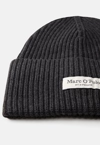 Pletená čierna čiapka s rebrovanou textúrou a prehnutým manžetovým okrajom, na ktorej je biela nálepka s textom "Marc O'Polo" a "EST. IN STOCKHOLM."
