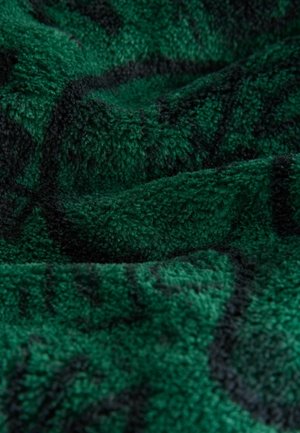 Zeleno teksturirano blago z mehkobno, plišasto površino, ki vsebuje temen vzorec. Material izgleda puhast in vabljiv.