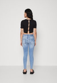 Black short-sleeve top with open back and button accents, paired with light blue skinny jeans, featuring a gradual fade and contouring fit.