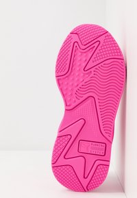 Semelle de chaussure rose vif avec motifs de bande de roulement texturés et texte "RUNNING SYSTEM" près du talon, positionnée à la verticale sur un fond blanc.
