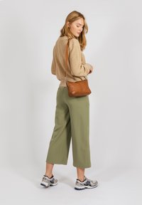 Maglione lavorato a maglia beige, pantaloni larghi verde oliva, borsa a tracolla in pelle marrone, scarpe da ginnastica argento con dettagli neri.