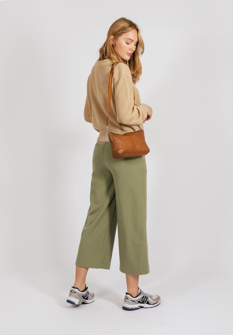Maglione lavorato a maglia beige, pantaloni larghi verde oliva, borsa a tracolla in pelle marrone, scarpe da ginnastica argento con dettagli neri.