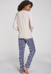 Light pink long-sleeve top paired with blue-patterned pajama pants featuring white and cream abstract shapes. Soft, casual fabric.