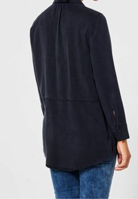 Námořnická košile s dlouhým rukávem, hladkou texturou, manžetami na knoflíky a zakřiveným lemem. Zadní strana má centrální sklady pro lepší splývavost.