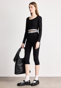 Μαύρο ραβδωτό τοπ με μακριά μανίκια συνδυασμένο με εφαρμοστά κολάν καπρί. Λευκή λογότυπη ζώνη και μαύρη δερμάτινη τσάντα ώμου με φαρδιά λουρί. Μαύρες μοκέτες με κάλτσες.