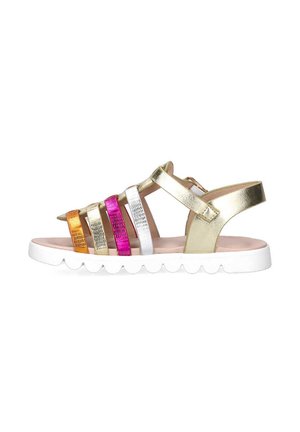 Sandalias metálicas doradas con tiras multicolores (dorado, naranja, plata, rosa, blanco) y una suela blanca con borde festoneado. Diseño de espalda abierta.
