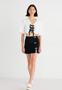 Top branco curto com atacadores de fita preta, combinado com uma saia mini preta com detalhes de laços brancos e recortes.