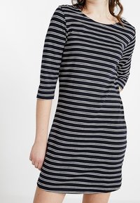 Marinblå klänning med vita horisontella ränder, trekvartslånga ärmar, rund halsringning och mjukt, stretchigt tyg. Mitten av låret längd.