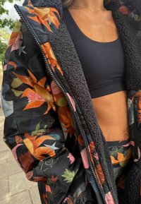 Tikkimust jakk lillemustritega oranžis, roosas ja rohelises, millel on kohev vooder ja tõmblukk. Allosas must lühike top.