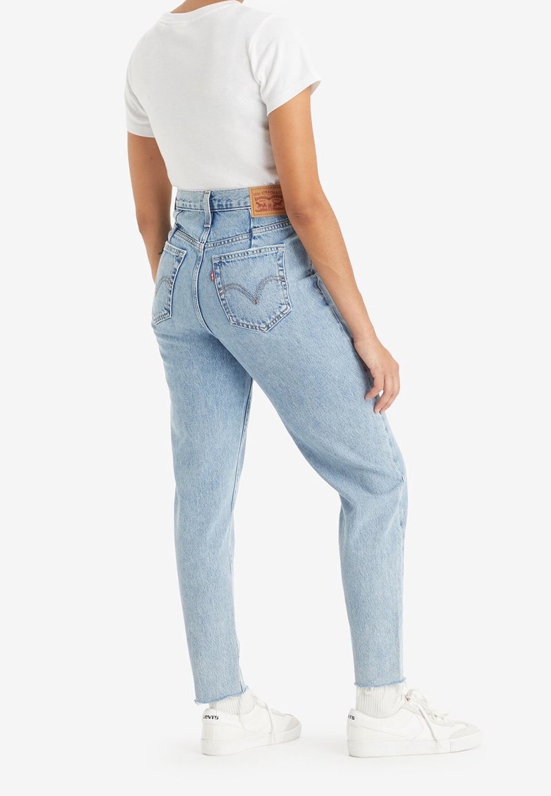 Ljust blå högmidjade jeans med tapered passform, med sydda bakfickor, fransade fållar och en lädermärke vid midjan.