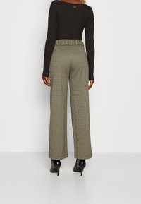 Haut noir à manches longues associé à un pantalon à jambes larges à motif crème et noir. Tissu texturé avec une ceinture élastique. Talons hauts noirs.