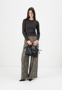 Czarny dopasowany top z długim rękawem, zestawiony z szerokimi spodniami w leopardzie wzory. Modelka trzyma czarną torebkę teksturowaną z akcentami w postaci węzła.