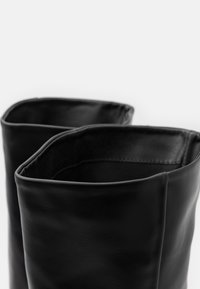 Bottines en cuir noir avec un bord supérieur carré, une texture lisse et un design minimaliste, affichant une apparence élégante et moderne.