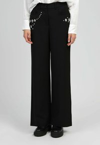 Pantalons noirs à jambes larges avec des embellissements en argent décoratifs sur les poches. Fabriqués en tissu lisse, avec une coupe décontractée et une taille classique.