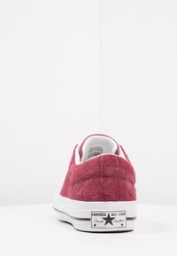 Red suede low-top sneaker with white rubber sole and black logo on the heel. Features white stitching and a padded collar.
