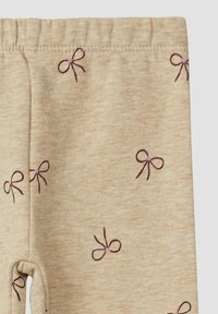 Beige stoffen broek met elastische tailleband, versierd met kleine paarse geborduurde strikjes verspreid over de stof.