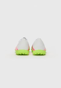 Vue arrière de chaussures de sport avec une tige blanche et des accents roses, et une semelle extérieure verte brillante, mettant en avant un design élégant et un matériau texturé.