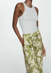 Grijze mouwloze top gecombineerd met een hoge taille, groene broek met bloemenprint, brede pijpen, een strikceintuur en zijzakken.