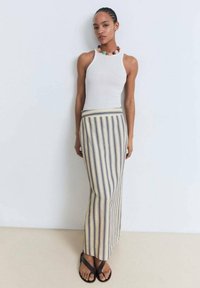 Witte geribde tanktop gecombineerd met een gestreepte maxi rok in beige en marineblauw. De rok heeft een aansluitende tailleband en valt tot aan de enkel. Zwarte teenslippers.