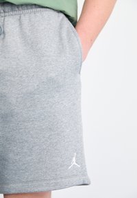 Grå bomullsblandning shorts med elastisk midja, sidfickor och en vit logotypaccent på fållen. Slät textur, knälång passform.