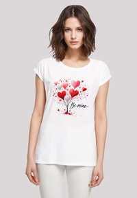 White cotton t-shirt featuring a colorful heart tree design in red and pink, with the handwritten text "Be mine" underneath. Short sleeves.