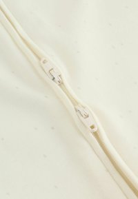 Kremasta tkanina z drobnim pikčastim vzorcem, s centralno dvosmerno zadrgo z belimi plastičnimi potegi. Gladek in mehak material.