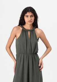 Vestido verde-oliva feito de um tecido suave, com decote trançado, abertura em forma de olho-chave e uma cintura elástica para um ajuste confortável. Design longo e fluido.
