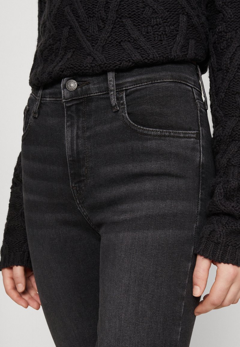 Jean noir taille haute en denim avec une texture lisse, présentant une fermeture à bouton à l'avant et des poches latérales. Accentué par un léger délavage.
