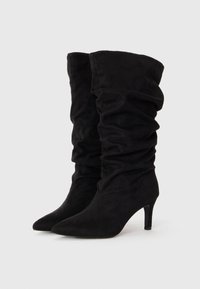 Bottes hautes en suède noir avec un design décontracté, bout pointu et finition texturée. Talons d'environ 7,5 cm.