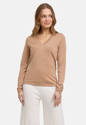 Suéter beige de cuello en V en un punto ligero, con mangas largas y un ajuste relajado, combinado con pantalones blancos de punto acanalado.